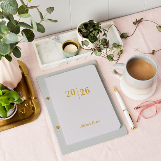 martha brook personalised stationery personalised analogue 2026 weekly diary in pebble grey on a pink desk with a mug of tea and pink framed reading glasses