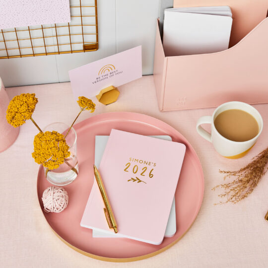 martha brook personalised stationery personalised bloom 2026 weekly diary in blush pink on a pink desk with dried yellow flowers and a mug of tea