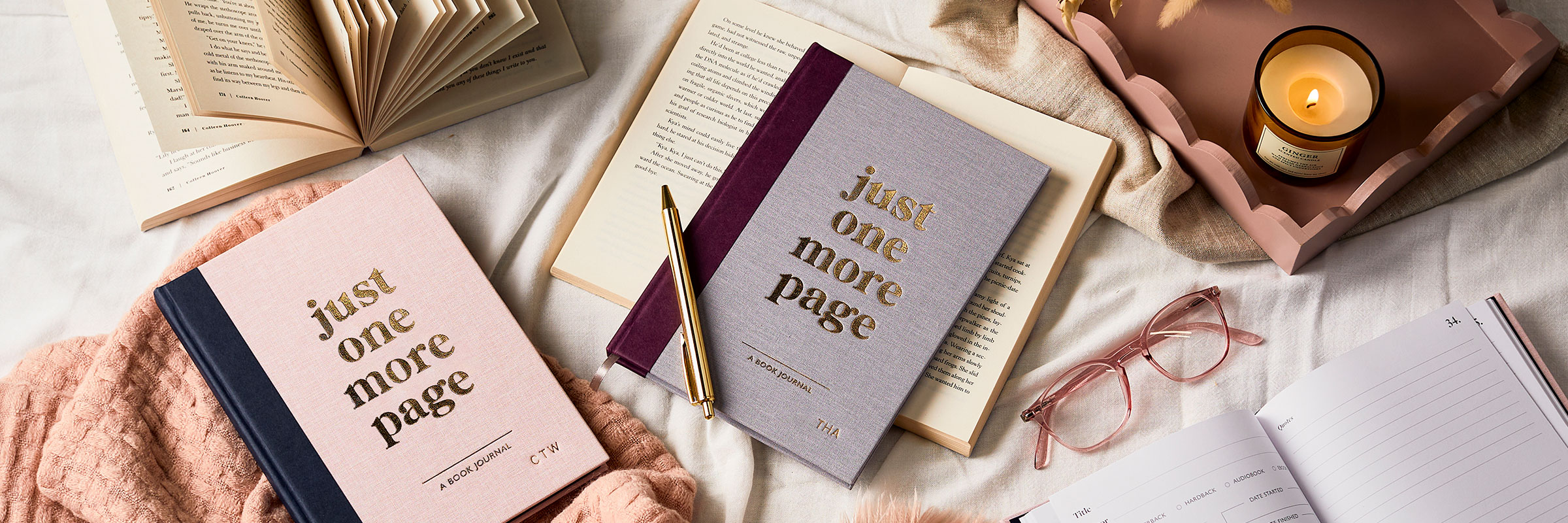 Martha Brook australia personalised stationery winter stationery picks book journal on a bed with a pink blanker, a pink wooden tray with a lit candle on it sits in the top right. The books have a gold pen on top of it and they are surrounded by open novels