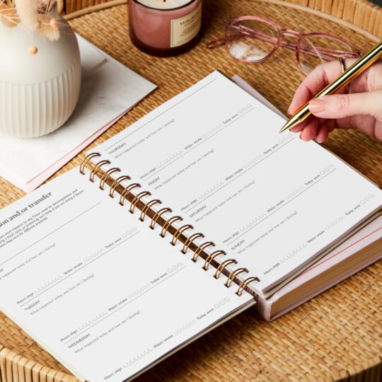 martha brook personalised ivf journal on side table with a candle open on the protocol page with hand writing in it